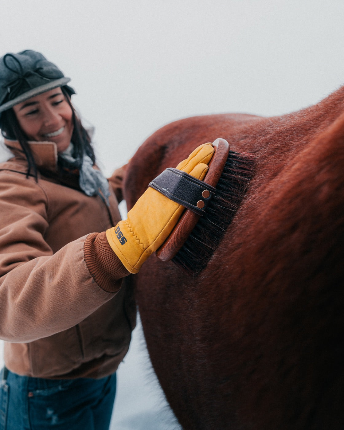 Woman brushing horse in snow with yellow gloves
